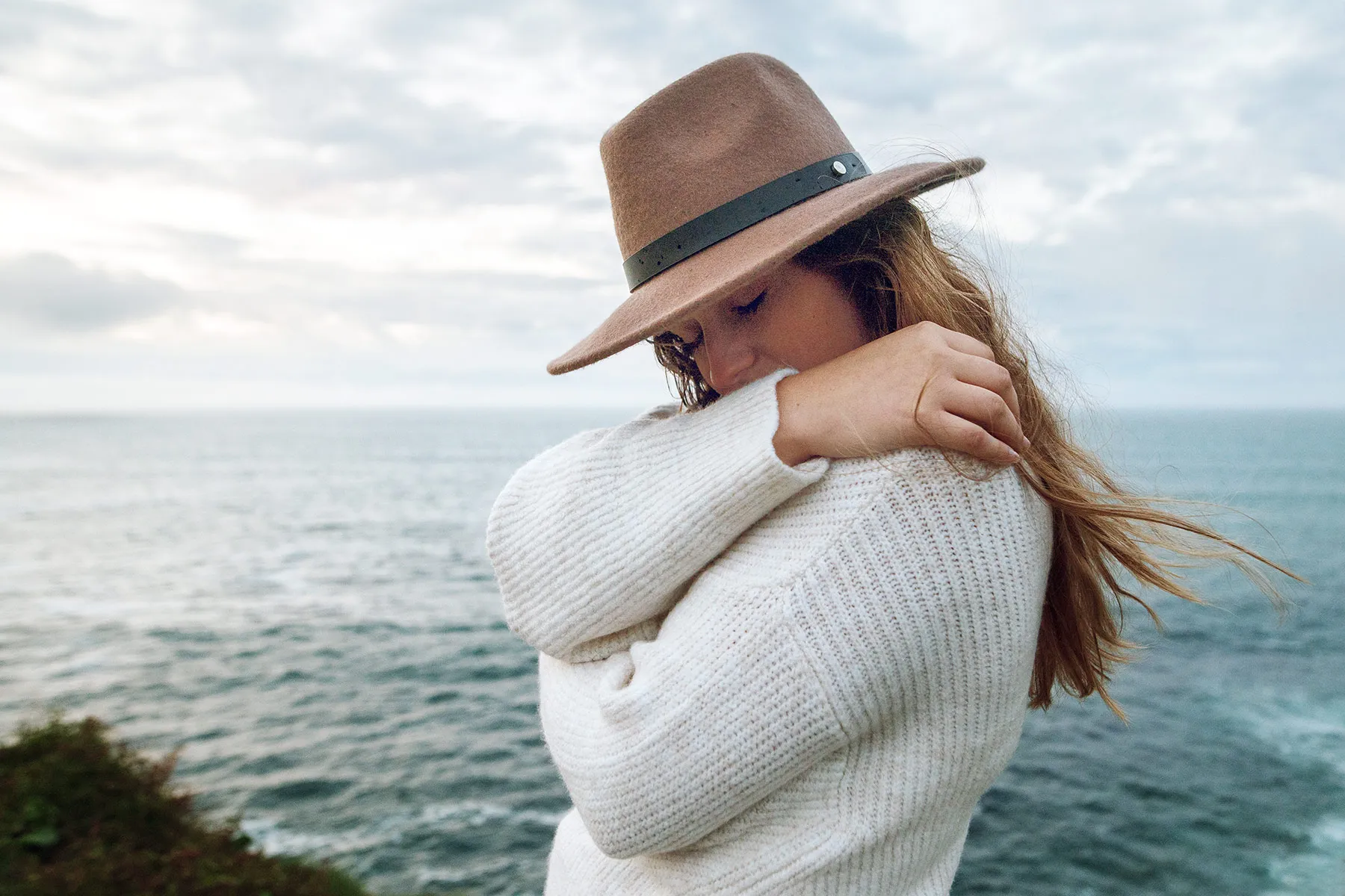 photo of young woman by sea hugging self