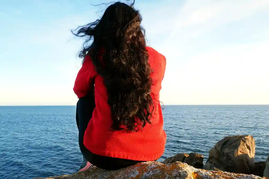 photo of woman sitting on a rock by the ocean