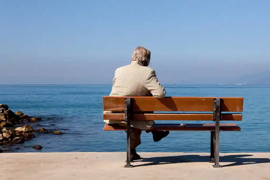 photo of man sitting alone on bench by water
