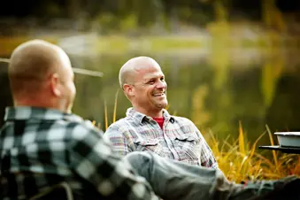 photo of man sitting with friends by lake smiling
