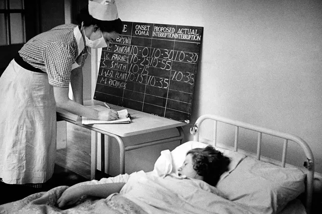A nurse checks on a psychiatric patient who lies in a state of insulin-induced coma. To break the coma, a dose of sugar is administered.
